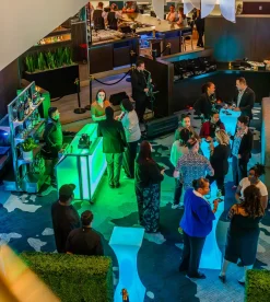 Instalación de alquiler de barra portátil iluminada Signature 62 en la recepción de un hotel corporativo con iluminación LED y servicio profesional. LED portable bar rentals with green and blue lighting at upscale corporate hotel event, featuring multiple modular bar stations with professional bartenders serving guests