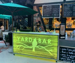 portable-bar-77-outdoor-restaurant-patio-bar Portable Bar 77 setup as a sidewalk patio bar featuring custom rustic wood branding and green LED lighting, expanding outdoor beverage service for a restaurant