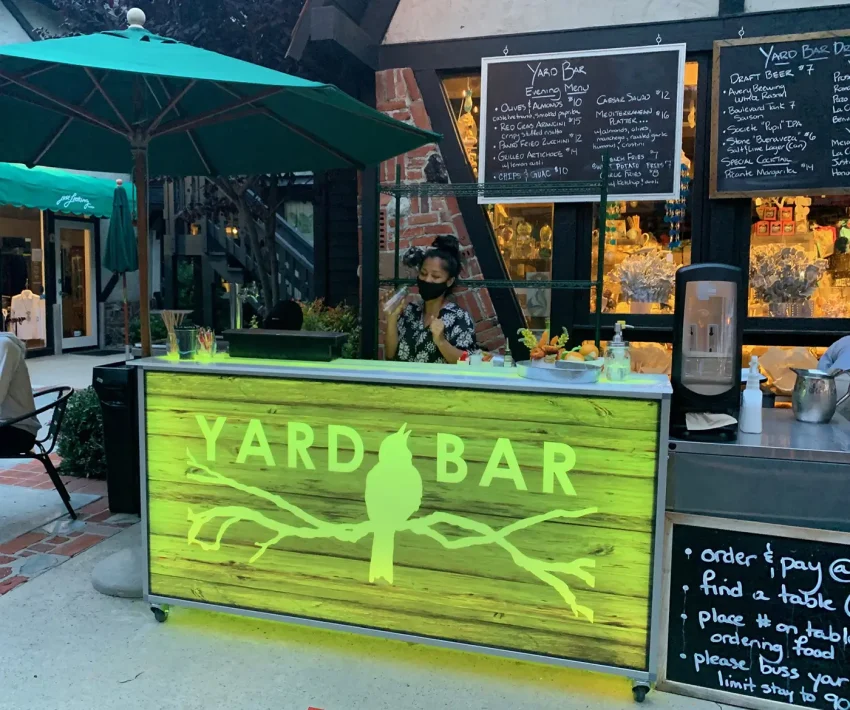 portable-bar-77-outdoor-restaurant-patio-bar Portable Bar 77 setup as a sidewalk patio bar featuring custom rustic wood branding and green LED lighting, expanding outdoor beverage service for a restaurant