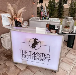 Fusion 48 Portable Bar - Custom LED Branding for Mobile Bartenders Fusion 48 portable folding bar setup outdoors for a birthday event, featuring The Twisted Trotter custom logo on the backlit LED front panel with mobile bartending supplies.